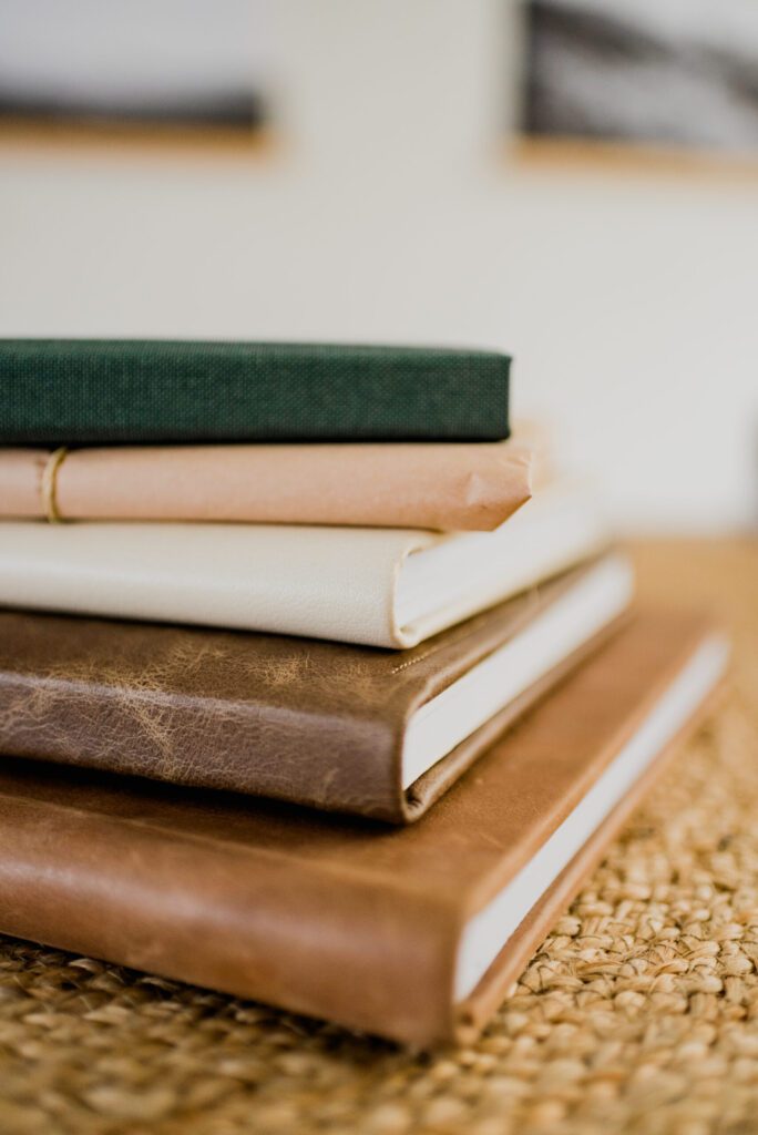 Een stapel stijlvolle fotoalbums op maat gemaakt in drenthe met diverse materialen en kleuren, variërend van leer tot linnen, zorgvuldig geplaatst op een rustieke ondergrond.