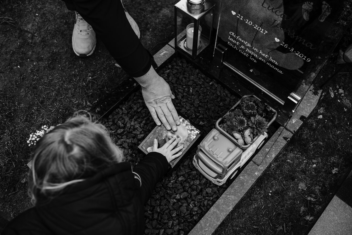 Herdenking: Een ontroerend moment bij een grafsteen waar een kind en een ouder een herdenkingsobject aanraken.